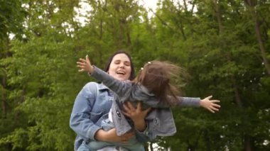 Mutlu genç anne ve küçük kız yazın açık yeşil parkta Uluslararası Anneler Günü 'nde oynayıp gülüyorlar 