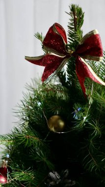 Yeşil bir Noel ağacında kırmızı bir fiyonk, Yılbaşı arifesinde beyaz fenerlerin beyaz arka planı.