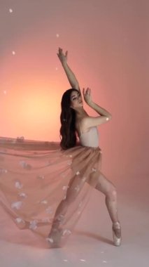 Genç bir kadın, dans eden bir balerin kız, fotoğraf çekiminde fotoğraf stüdyosunda poz veriyor, kollarını ve parmaklarını yavaşça pembe arka planda hareket ettiriyor, yavaş çekim, orta. Kahverengi saçlı kadın, uzun saçlı.