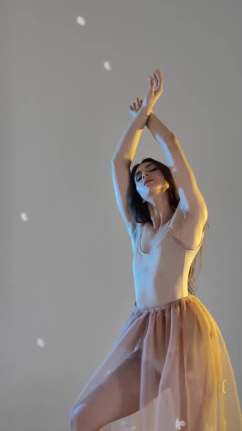 一个年轻的女子 一个芭蕾舞女 在一间工作室的灰色背景上轻柔地移动着她的胳膊和手指 动作缓慢 棕色头发的女士 垂直录像 — 图库视频影像