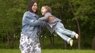 Mutlu genç anne ve küçük kız yazın açık yeşil parkta Uluslararası Anneler Günü 'nde oynayıp gülüyorlar 
