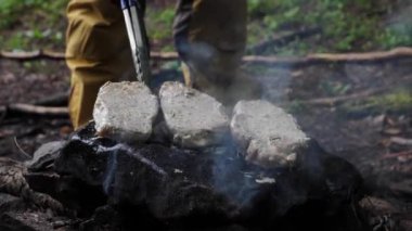 Bir el adamı et pişirir, ormandaki bir kayanın üzerinde biftek hazırlar yakın plan bir yürüyüş. Tarlada yemek pişirmek için ateşte yakılan şenlik ateşi.