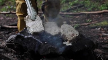 Bir el adamı et pişirir, ormandaki bir kayanın üzerinde biftek hazırlar yakın plan bir yürüyüş. Tarlada yemek pişirmek için ateşte yakılan şenlik ateşi.