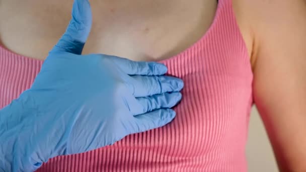 医療用手袋の哺乳類学者は 国際がんデーのクリニックで乳がんの若い女性の胸をチェックします クローズアップ — ストック動画
