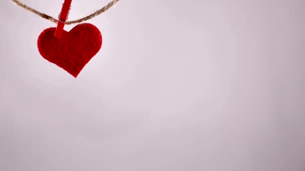 白いバックグラウンドに対してロープからぶら下がっている赤い感じの心臓は 焦点にあります バレンタインデー 心臓は横から横へ優しく揺れる — ストック動画