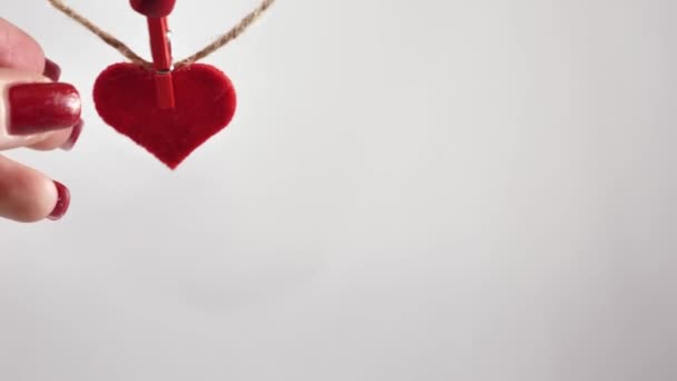 女性の手は 国際バレンタインデーの白い背景に木の布を使用して愛の装飾的な赤い心臓をジュートロープに添付します 世界の心臓の日 — ストック動画