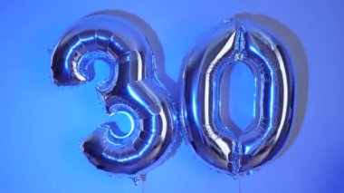 Doğum günü kutlaması için 30 numara şeklinde iki gümüş balon. Renkli bir arkaplanda yakın plan