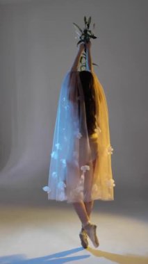 Genç bir kadın, dans eden bir balerin kız, yavaşça kollarını ve parmaklarını bir stüdyonun beyaz arka planında hareket ettiriyor, yavaş, orta boylu. Uzun saçlı, kahverengi saçlı kadın. Dikey