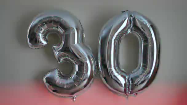 30歳の誕生日を祝うために ナンバー30の形をした2つの銀の風船 色付きの背景にクローズアップ — ストック動画
