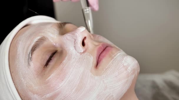 Cosmetologist Profissional Aplica Uma Máscara Branca Cara Cliente Fêmea Com — Vídeo de Stock