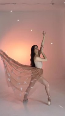 Genç bir kadın, dans eden bir balerin kız, fotoğraf çekiminde fotoğraf stüdyosunda poz veriyor, kollarını ve parmaklarını yavaşça pembe arka planda hareket ettiriyor, yavaş çekim, orta. Kahverengi saçlı kadın, uzun saçlı.