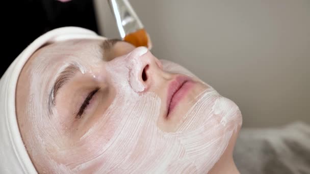 専門の化粧品学者はブラシが付いている女性の顧客の表面の白いマスクを クローズアップ加えます — ストック動画