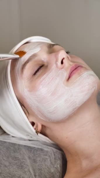 Professionelle Kosmetikerin Trägt Eine Weiße Maske Auf Das Gesicht Einer — Stockvideo