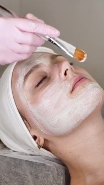 Cosmetologist Profissional Aplica Uma Máscara Barro Branco Rosto Cliente Feminino — Vídeo de Stock
