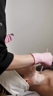 Profesyonel kozmetik uzmanı, kadın bir müşterinin yüzüne beyaz kilden bir maske takıyor.