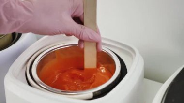 Bir tüy dökücü ustası portakal tanecikli balmumunu ahşap bir spatulayla eritiyor. Yakın plan.