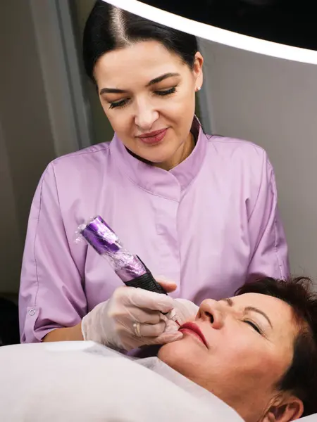 Kalıcı makyaj sanatçısı 50 yaşını geçmiş güzel bir kadına müşterilerin yüzündeki güzellik salonunda dövme yaptırıyor. Dikey