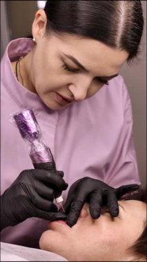 Kalıcı dudak makyajı. 50 yaşını geçmiş güzel bir kadın. Bir güzellik salonunda. Yakından bir güzellik uzmanı yüzüne dövme yaptırıyor. Dikey