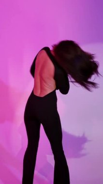 Mor ışıklı arka planda Bachata Lady Style, siyah kıyafetle dans eden genç esmer beyaz kadın. dikey, genel olarak yakın plan