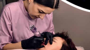 Kalıcı dudak makyajı. 50 yaşını geçmiş güzel bir kadın. Bir güzellik salonunda. Bir güzellik uzmanı yüzüne dövme yaptırıyor.. 
