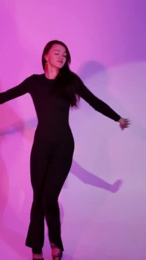 Mor ışıklı arka planda Bachata Lady Style, siyah kıyafetle dans eden genç esmer beyaz kadın. dikey, genel olarak yakın plan