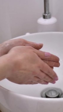 Kadın bir güzellik uzmanı ellerini lavaboda dezenfektan sabunla yıkıyor. dikey, yakın plan