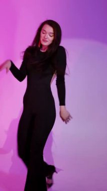 Mor ışıklı arka planda Bachata Lady Style, siyah kıyafetle dans eden genç esmer beyaz kadın. dikey, genel olarak yakın plan