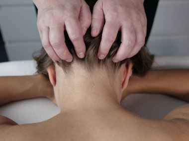 Bir terapistin elinin, beyaz bir spa masasında yüz üstü yatan birine rahatlatıcı kafa ve kafa masajı yaparken çekilmiş yakın plan fotoğrafı.
