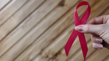 Katlanmış kırmızı farkındalık kurdelesini ahşap arka planda tutan, dayanışmayı sembolize eden elin yakın çekimi, Dünya AIDS Günü veya kalp sağlığı farkındalığını sembolize eden.