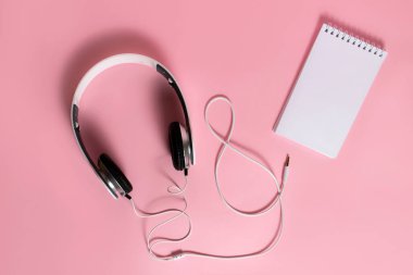Kulaklıklar ve pembe arka planda boş not defteri. Üst görünüm, düz arkaplan