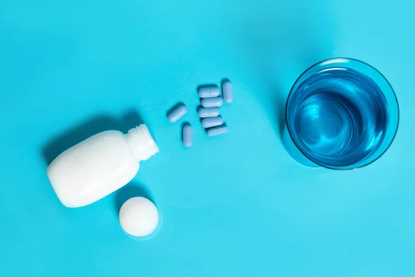 Pílulas Medicina Azul Uma Garrafa Branca Copo Água Fundo Azul — Fotografia de Stock