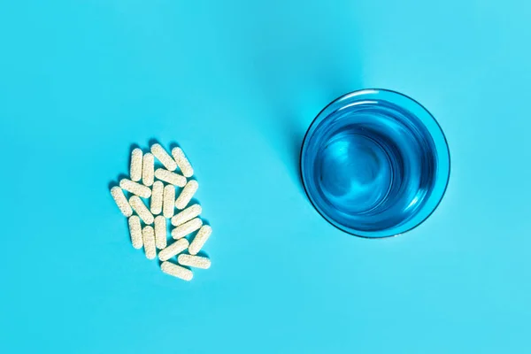 Pílulas Cápsulas Copo Azul Água Fundo Azul Visão Superior Conceito — Fotografia de Stock
