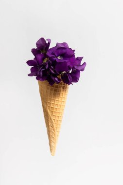 Ice cream cone with wild violets on white background. Spring flowers concept.
