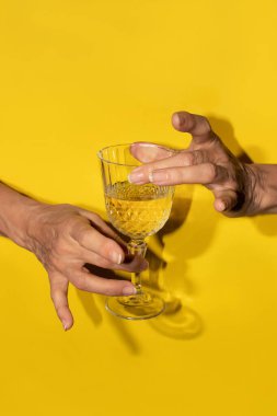 Sarı arka planda beyaz şarabı bardakta tutan iki el.