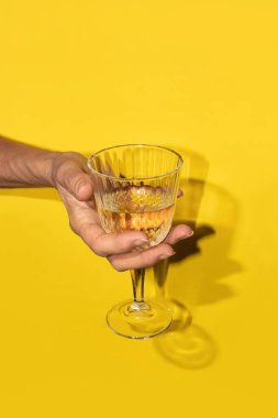 Beyaz şarabı sarı arka planda bir bardakta tutan el.