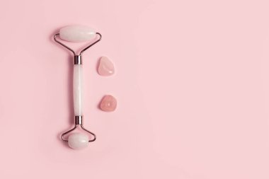 Pembe arka planda Jade Roller ve pembe kristal kuvars taşları. Düz yatış, üst görünüm.