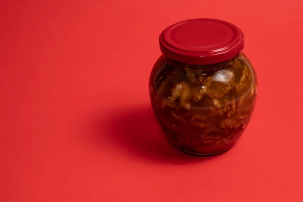 stock image Jar of walnuts in honey on red background