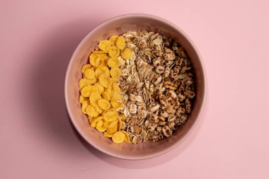 Pembe bir kasede çeşitli kahvaltı gevrekleri. Mısır gevreği rulo yulaf ve buğday. Pembe arkaplan.