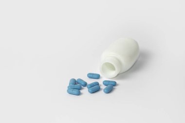 Beyaz arka planda beyaz hap şişesinde mavi haplar.