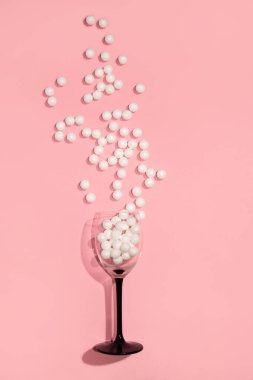 Wine glass with white shiny beads on a pink background. Creative minimal party concept.