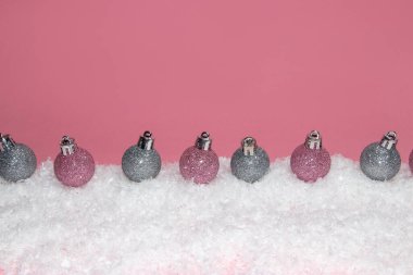 Christmas tree ornaments on snow. Pink background. Christmas or New Year concept.