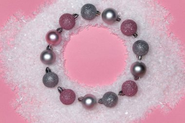 Pink and silver ornaments wreath with snow on pink background. Christmas concept. Flat lay top view circle frame.