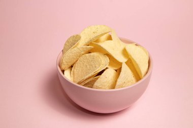 Pembe arka planda bir kasede patates cipsi. Üst görünüm.