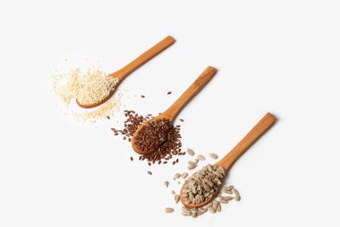 Susam tohumları keten tohumları ay çekirdekleri tahta kaşıklarda beyaz arka planda