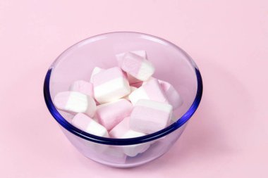 Pembe ve beyaz lokum küpleri pembe arka planda mavi cam bir kasede.