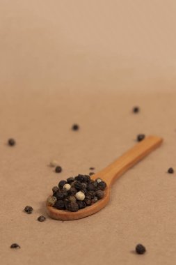 Kahverengi arka planda ahşap kaşıkta siyah biber.