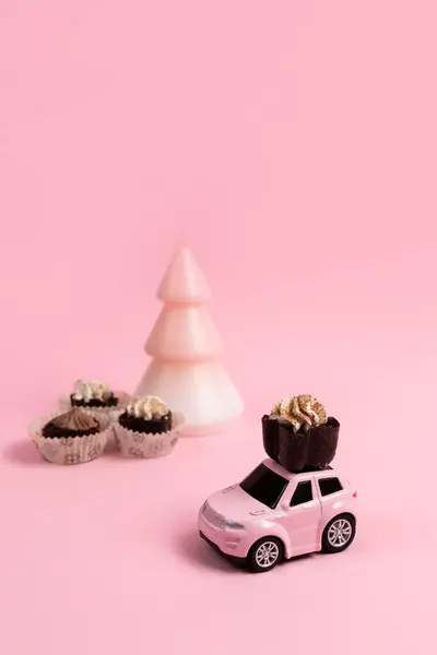 Pink toy car with chocolate candies with cream and pink tree candle on a pink background