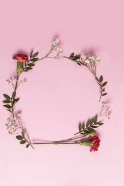 Kırmızı karanfillerden, beyaz çiçeklerden ve pembe arkaplandaki yapraklardan oluşan yuvarlak çerçeve. Üst manzara, düz uzanma.