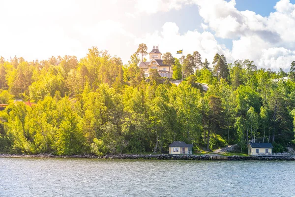 Grand residential villa situated on a forested hill overlooking the coastline of the Swedish archipelago. The view is from the sea on a clear summer day