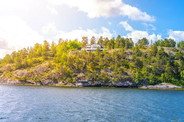 Noble rural villa on a forested hill above a bay on a clear summer day. View from the sea. Stockholm Archipelago, Sweden